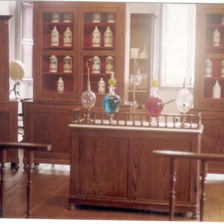 Posicionamento da Farmácia Magalhães Gomes com extratos, tinturas e vidrarias na 1ª sala e sua reorganização na 2ª sala.